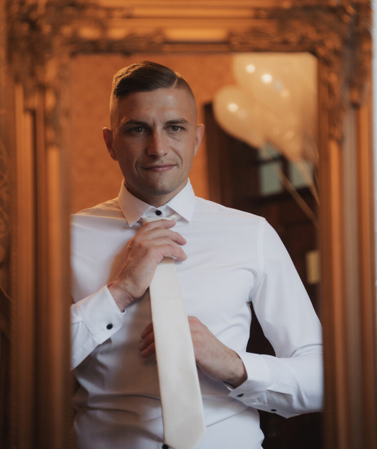 Ženich si váže kravatu před zrcadlem